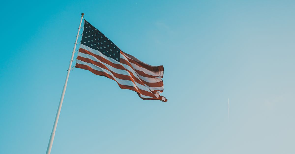 A low angle shot of the American flag waving against a clear blue sky, symbolizing patriotism.